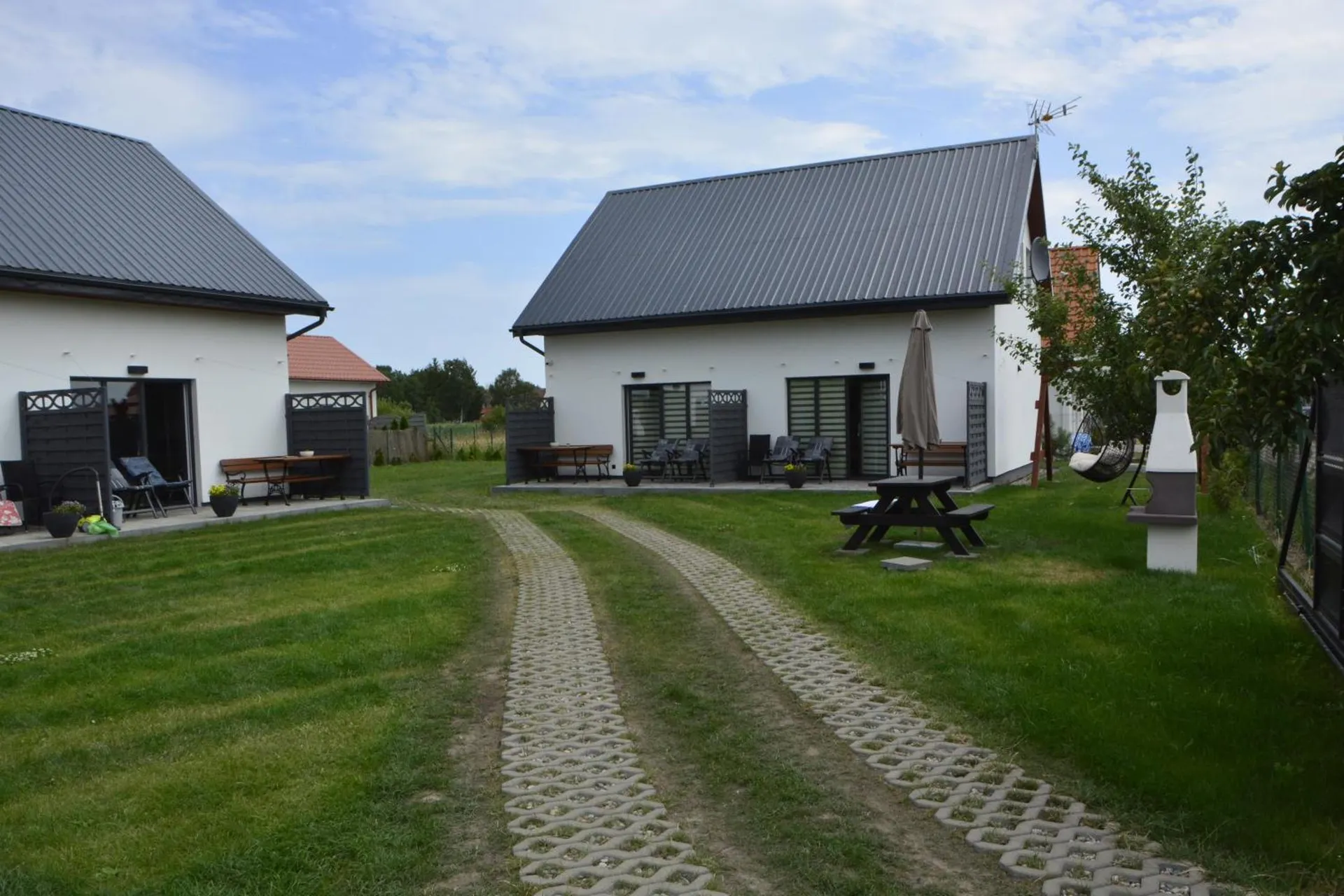Ogród między domkami — murowany grill, ścieżka z kostki i wiszący fotel pod jabłonią