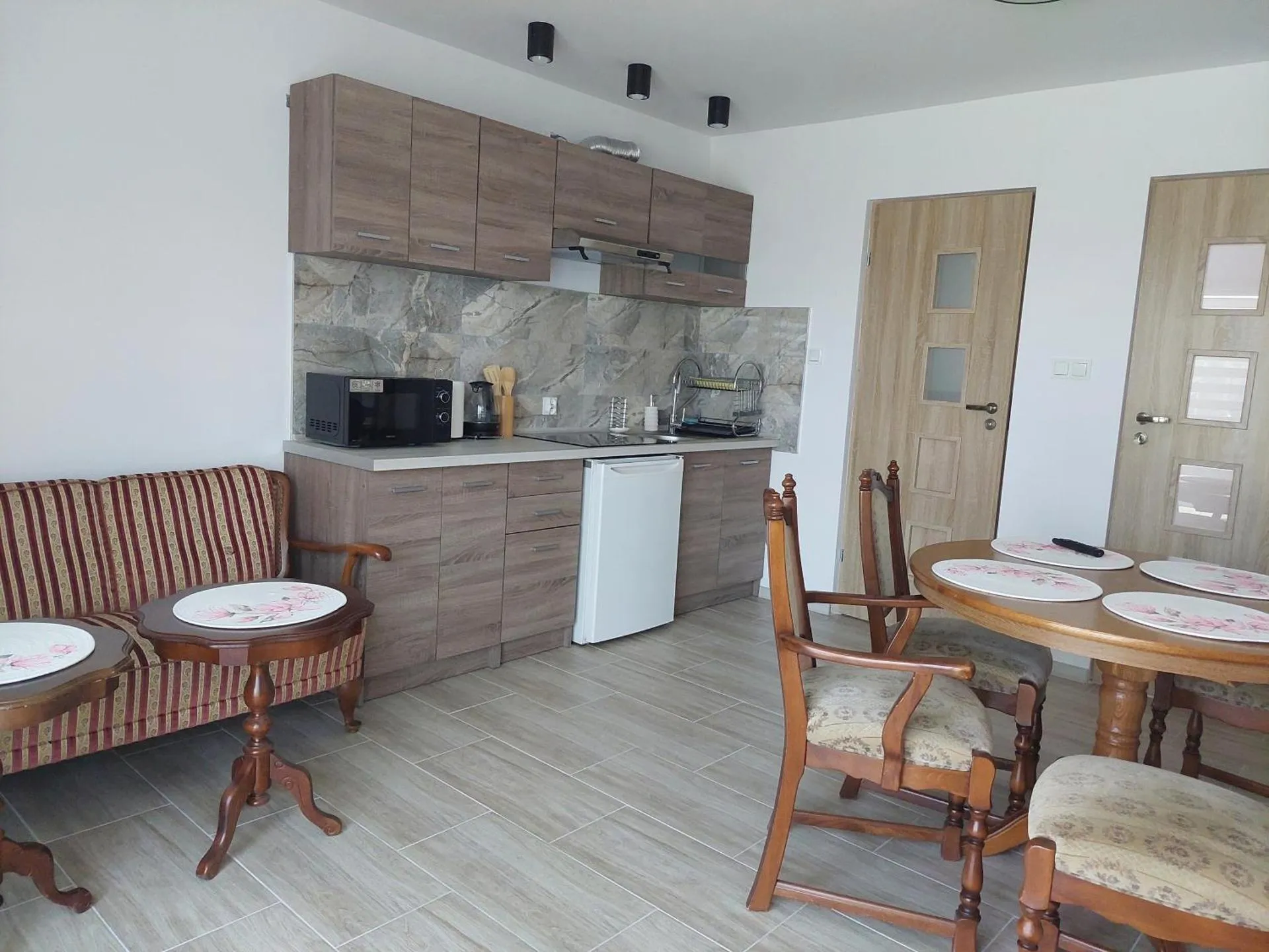 Część dzienna — aneks kuchenny w ciemnym drewnie, sofa w pasy i owalny stół